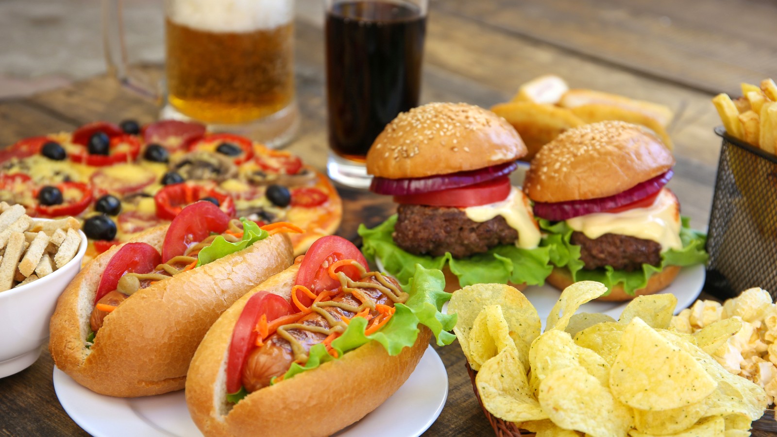 Photo showing various fatty foods: pizza, burgers, hot dogs, chips, as well as soft drink and beer